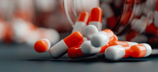 Pills spilling from an open jar onto a wooden table surface.