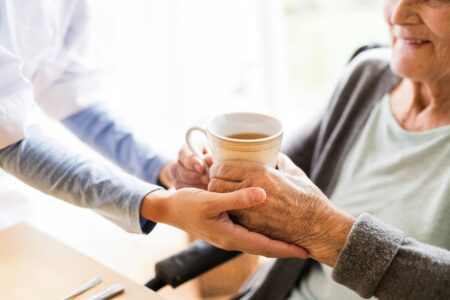 A nurse offers a cup of coffee to an elderly woman, fostering a warm and caring interaction in a healthcare setting.