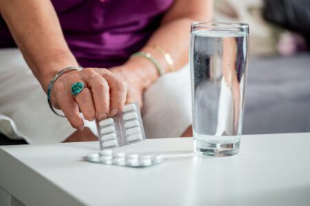 A woman holds a glass of water in one hand and a pill in the other, preparing to take her medication.