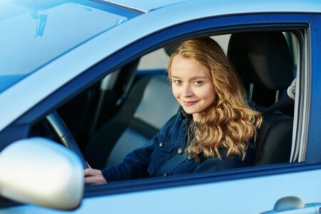 A young woman sits in the driver's seat of a car, focused and ready to drive.