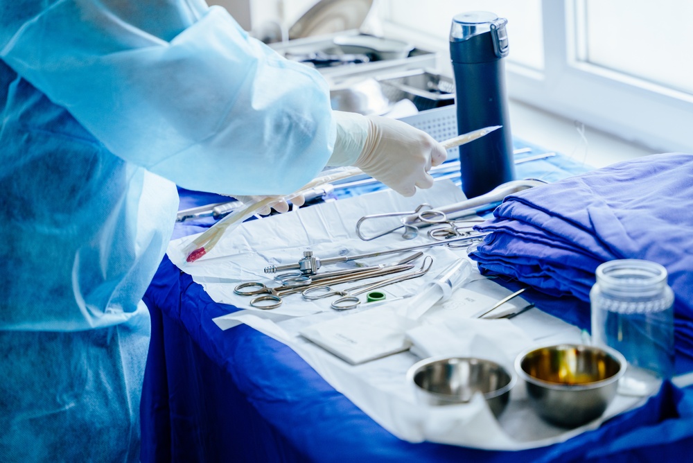 Gowned and gloved person arranging surgical instruments on a draped table