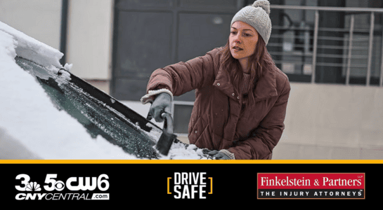 Woman in a knit hat and brown coat scraping snow off a car windshield; logos for CNYCENTRAL.com, DRIVE SAFE, and Finkelstein & Partners The Injury Attorneys
