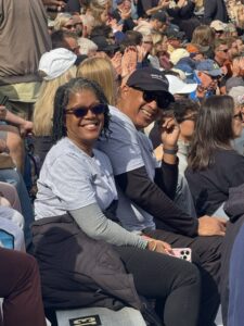 Woman and man smiling together in the stands at a sporting event, surrounded by cheering fans