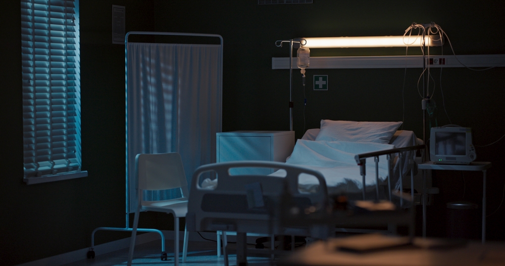 Empty hospital bed with an IV stand in a dark hospital room